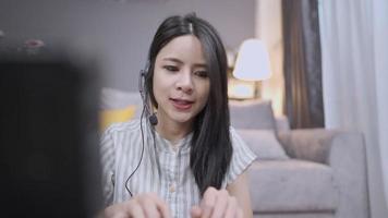 Young asian female operator with headset microphone consulting on client problems and recording information on computer, live chat with staff from home, customer convenience service, relaxing working video