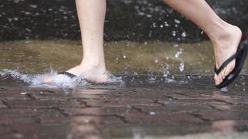 lage hoek schot van voeten dragen flipflop rennen op de zware stromende regendag, overstroomde straat, stormachtige tyfoon moessonseizoenen, natte voeten haasten op de waterplas, kletsnatte sandalen op de regenachtige dag