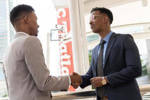 bienvenido a nuestro equipo. jóvenes modernos con ropa informal elegante dándose la mano. dos hombres de negocios sonrientes dándose la mano. dos hombres de negocios confiados dándose la mano en el exterior de la oficina. foto