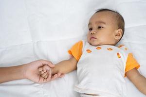 madre con bebé sosteniendo la mano sobre un colchón blanco foto