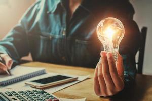 business woman hand holding light bulb in office. conept saving energy photo