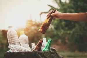 mano sosteniendo el vidrio de la botella de basura poniendo en la bolsa de reciclaje para limpiar foto