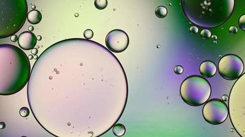óleo de comida colorido abstrato deixa cair bolhas e esferas fluindo na superfície da água, macro videografia