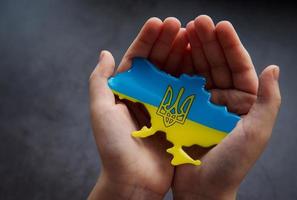 Hands holding the shape of Ukraine border with color flag photo