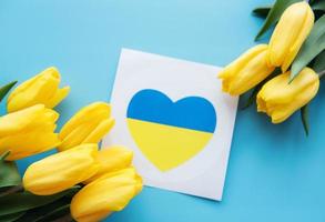 Card with a heart in the colors of the Ukrainian flag and yellow tulips on a blue background photo