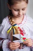 una niña ucraniana vestida con ropa tradicional sostiene una paloma de paz de papel en sus manos foto