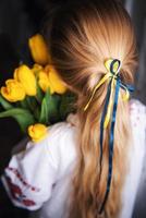A little Ukrainian girl in traditional clothes holds a yellow tulips in her hands photo