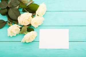 Frame of colorful roses on blue wooden background with paper card and copy space. Top view and selective focus. Mock up photo