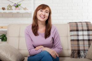 Beautiful and cute smiling middle age woman sitting on sofa. Home background. Happy menopause concept. photo