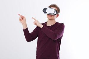 Excited young man in a VR headset, glasses pointing by fingers to the air. Virtual reality isolated on white background. Copy space and mock up photo