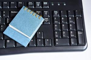 bloc de notas azul en el teclado negro. endecha plana, directamente arriba. foto