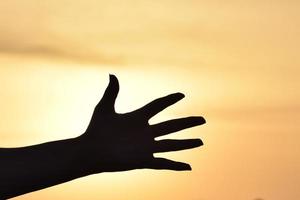 Silhouette of a hand over the sky at sunset photo