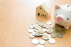 Selective focus of Piggy bank and wooden house on wood table with money coin.Saving plan to buy property, house. Personal financial concept for own a house. with copy space for text photo