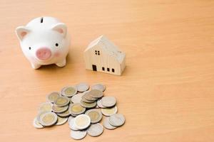 Selective focus of Piggy bank and wooden house on wood table with money coin.Saving plan to buy property, house. Personal financial concept for own a house. with copy space for text photo