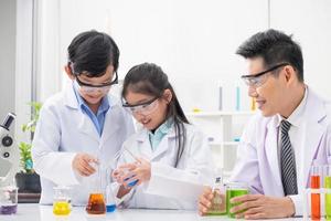 Young Asian boy and girl smile and having fun while learning science experiment in laboratory with teacher in classroom. Study with scientific equipment and tubes. Education concept. photo