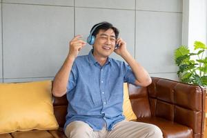 Senior Asian grandfather enjoy and feeling happy while listening music from wireless headphone that streaming music from smartphone or tablet device. Elderly retirement lifestyle with good health. photo