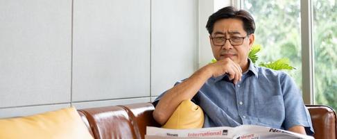 pancarta o foto panorámica de un anciano asiático que se ve serio mientras lee el periódico por la mañana en casa. estilo de vida interior de personas mayores que se ven estresados, infelices.