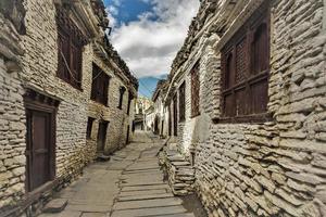 A narrow stone paved street in the village of Marpha lined with ancient, traditional whitewashed wood and stone houses on the Annapurna Circuit trail in the Nepal Himalaya.
