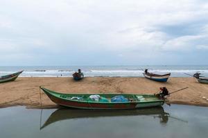 un barco de pesca de madera verde junto a un charco de agua en una playa de mahabalipuram.