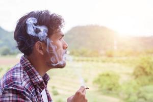 Hipster man smoking cigarette, standing behind a mountain. Among the fresh air in the morning. photo