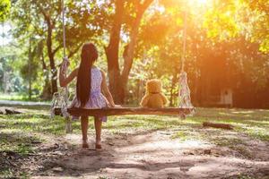 A little girl and teddy bear sitting on a swing. photo