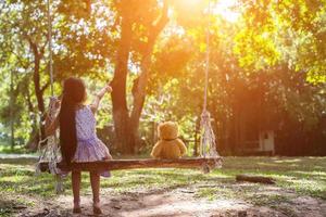 A little girl and teddy bear sitting on a swing. photo