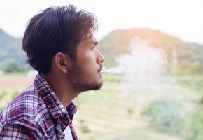 Hipster man smoking cigarette, standing behind a mountain. Among the fresh air in the morning. photo