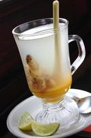A glass of warm ginger drink and lime. Decorated with lemon grass in the glass. clear. Placed on a saucepan plus a thin slice of lime photo