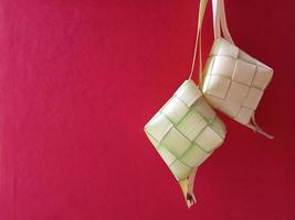 ketupat en indonesia es una forma de cocinar arroz con hojas de coco en forma de diamante. generalmente aparece en eid al-fitr. foto conceptual de ketupat sobre fondo rojo