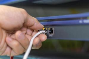 mano de un hombre que sostiene los cables de red para conectar el puerto de un conmutador para conectar la red de Internet, tecnología de comunicación conceptual foto