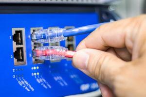 mano de un hombre que sostiene los cables de red para conectar el puerto de un conmutador para conectar la red de Internet, tecnología de comunicación conceptual foto