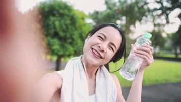 jovem mulher asiática tirando selfies durante o exercício no parque, segurando a garrafa de água, aproveite o compartilhamento de exercícios nas mídias sociais, tirando fotos sozinha após o treino, bem-estar de estilo de vida saudável