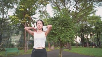 vista de seguimiento de una joven asiática deportiva de pelo negro corriendo a través de una cámara en un parque de la ciudad con un fondo verde público, una atractiva mujer bonita trotando en un entrenamiento al aire libre con un fondo de árboles video