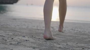 Rear view tanned legs walking on beach with a sunset in the edge of vanilla sky, tropical summer vacation, relaxing leisure activity on weekend, natural resources, beautiful relaxing cinematic vibe video