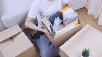 Young woman unboxing parcel carton box, sitting on floor moving inside new living room, good old memories, monthly rental, comfortable cozy new apartment, busy multitasking shore cleaning house day video