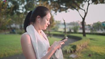 jovem asiática usa roupas esportivas usando smartphone enquanto se exercita no parque ao ar livre, ao pôr do sol, calma e relaxa vibe, estilo de vida de mulher solteira, condição médica de saúde, gadgets portáteis