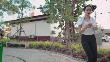 mujer joven activa corriendo y ocupada usando el teléfono a lo largo del lado de la calle, haciendo ejercicio en la ciudad, condición corporal para el cuidado de la salud de la mujer, en forma y firme, programa de rutina para quemar grasa, plan de dieta, música para hacer ejercicio video