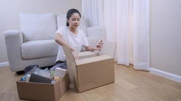 wide shot female buying new apartment, take stuff out of the parcel Storage box to arrange things, sit down couch behind, Multitasking works shore, Relocating moving in concept, stay at home
