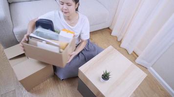 Young asian woman sorting things out of the parcel Cardboard box arrange, sit down on floor moving inside new living room, carton parcel container, Relocating move into new place, above top view video