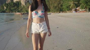 una modelo femenina segura de sí misma en un lindo bikini sexy y una planta corta blanca caminando alegremente en una famosa playa en vacaciones de verano, movimiento corporal femenino cerrado, confianza corporal, concepto de autoestima