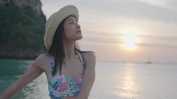 voyage côtier d'été, portrait sur une jeune femme asiatique étendant les bras et tournant son corps, exercice relaxant sur le front de mer, bain de soleil sur une plage privée avec une vue naturelle tropicale idyllique derrière video