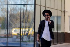 joven hombre feliz con traje negro y sombrero negro, concepto de hombre de negocios moderno foto
