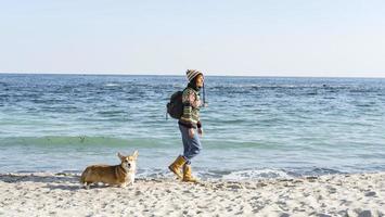 joven mujer feliz caminar con lindo perro corgi en la playa soleada de otoño foto