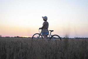 mujer joven con sombrero paseo en bicicleta en campos de trigo de verano foto