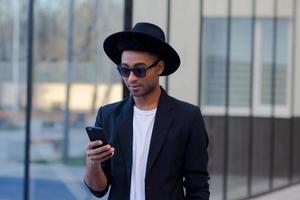 joven hombre feliz con traje negro y sombrero negro, concepto de hombre de negocios moderno foto