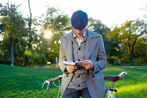 joven hipster masculino lee un libro en el parque de otoño foto