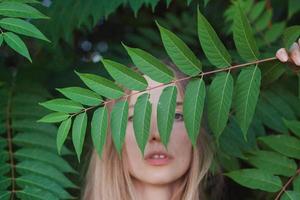 retrato de una bella joven con hojas verdes, una bella dama rubia con arbustos de primavera foto