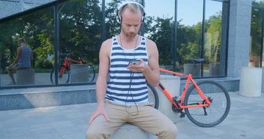 giovane bel maschio con bicicletta colorata e cuffie ascolta musica e cavalca per le strade estive