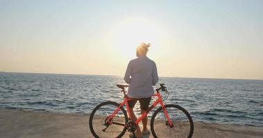 jovem macho bonito em roupas casuais passeio na bicicleta colorida na praia de manhã contra o belo pôr do sol e o mar