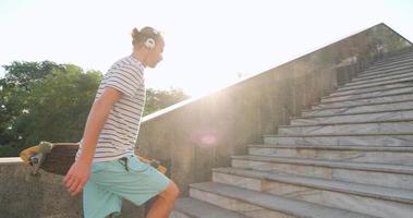 hübscher junger Mann mit Skateboard im Freien in der Stadt Musik mit Kopfhörern hören